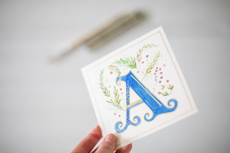 Een hand houdt een vierkant kaartje omhoog met een mooi geïllustreerde letter "A" op.