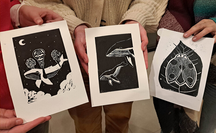 Drie paar handen houden elk een zwarte linoprint vast.