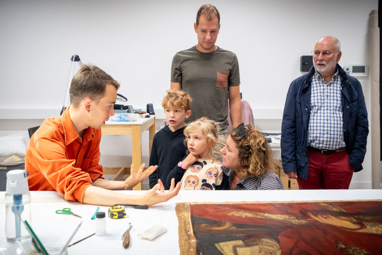 Een paar kindjes luisteren naar een depot medewerker die uitleg geeft bij een schilderij.