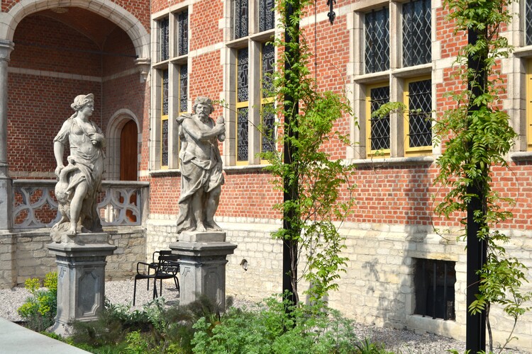 Twee standbeelden van Griekse figuren staan in een bloeiende museumtuin.