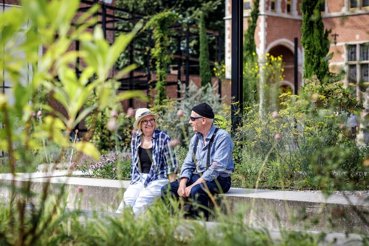 Twee mensen zitten op een betonnen bank in de museumtuin.