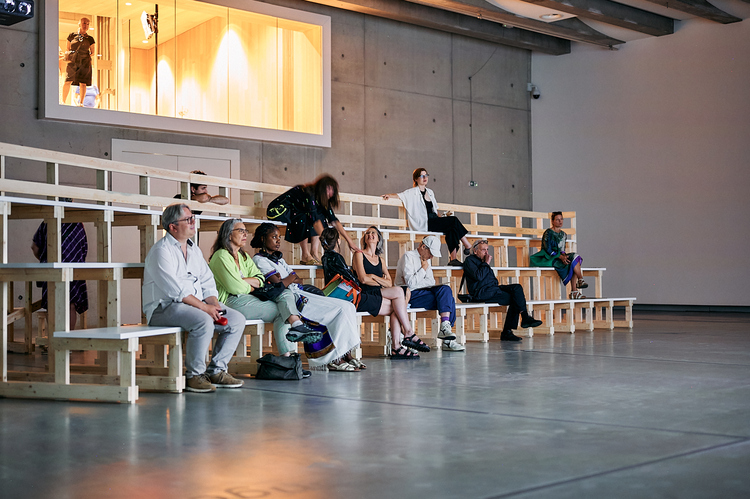 Een groep mensen zit op een tribune in een lege zaal.