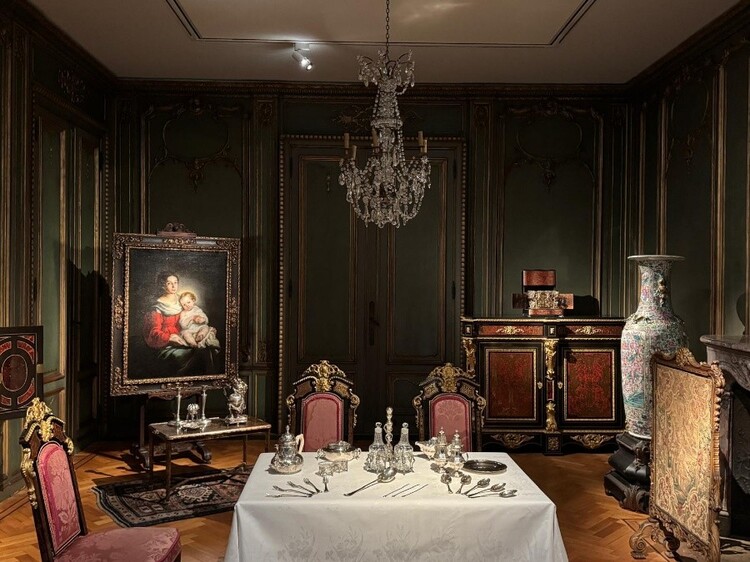 In een museumzaal staat een gedekte tafel met wit tafelkleed en zilveren bestek.