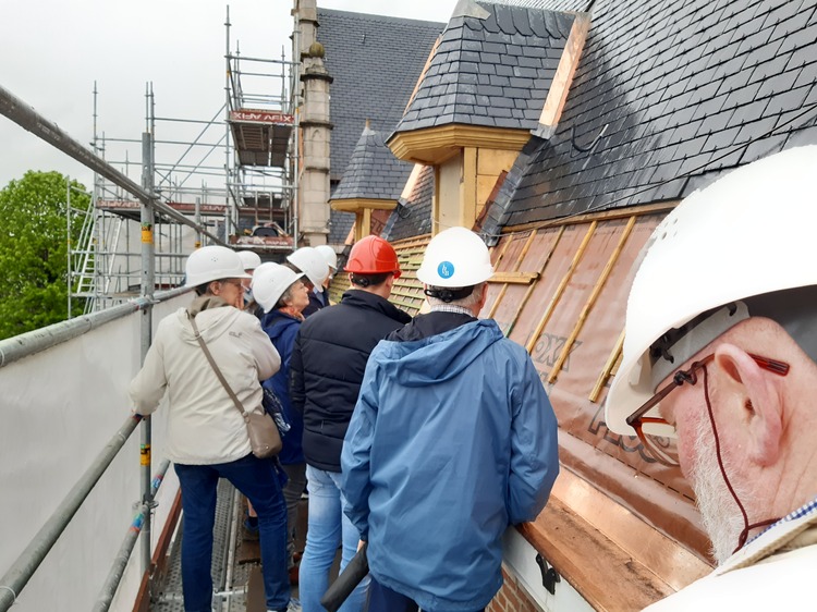 Groep mensen met harde helmen op stelling, ter hoogte van het dak van het stadspaleis.