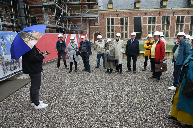 Vrienden van het museum staan in de tuin waar een medewerker uitleg geeft.