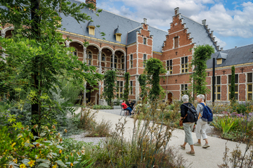 Twee mensen wandelen op een verhard pad in een weelderige stadstuin.
